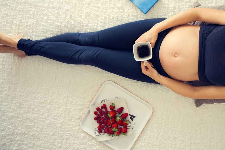 Schwangere trinkt Kaffee dazu Erdbeeren und Himbeeren