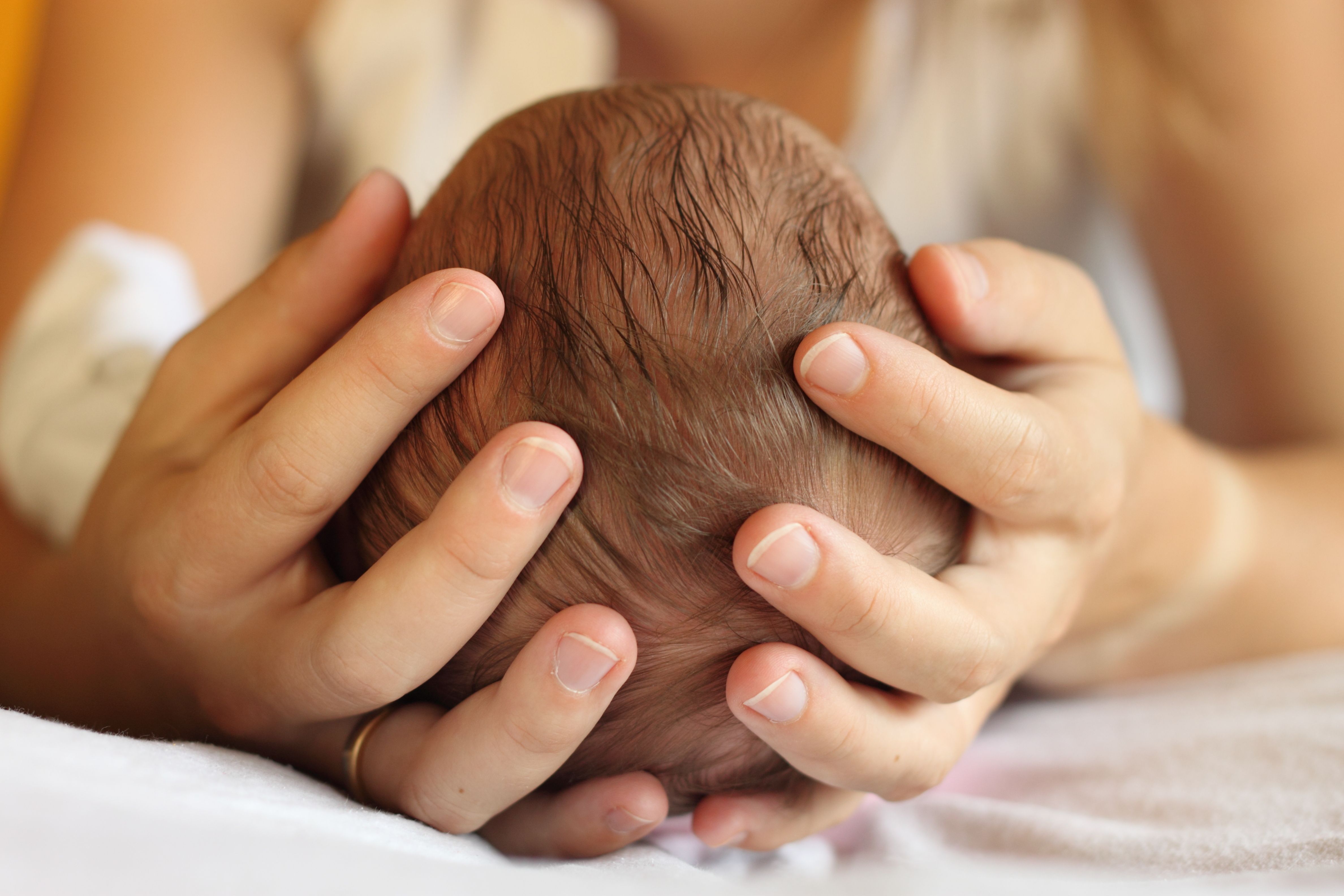 Kopf des Neugeborenen in Mutters Händen