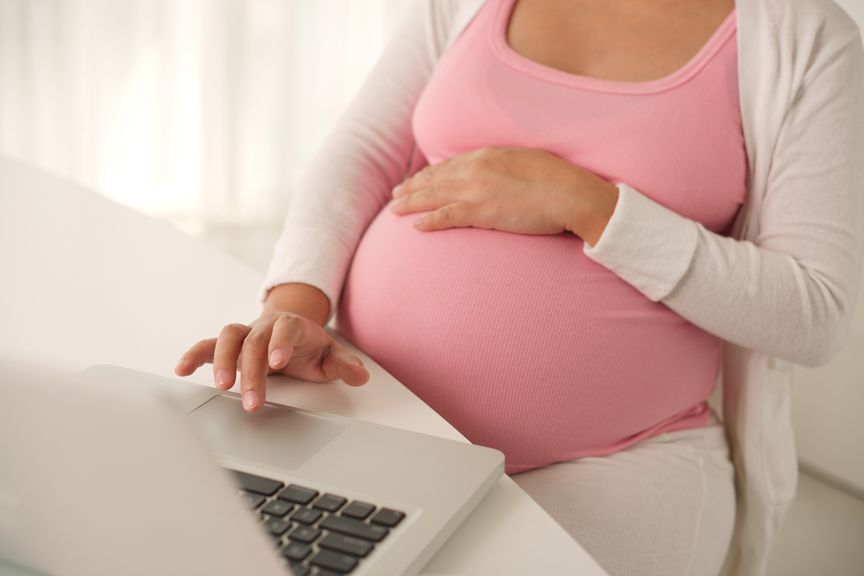 Schwangere mit Laptop am Tisch sitzend