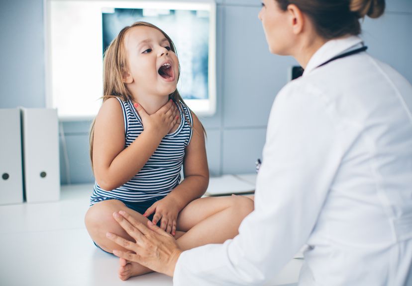 Kinderärztin schaut in den geöffneten Mund eines Kindes