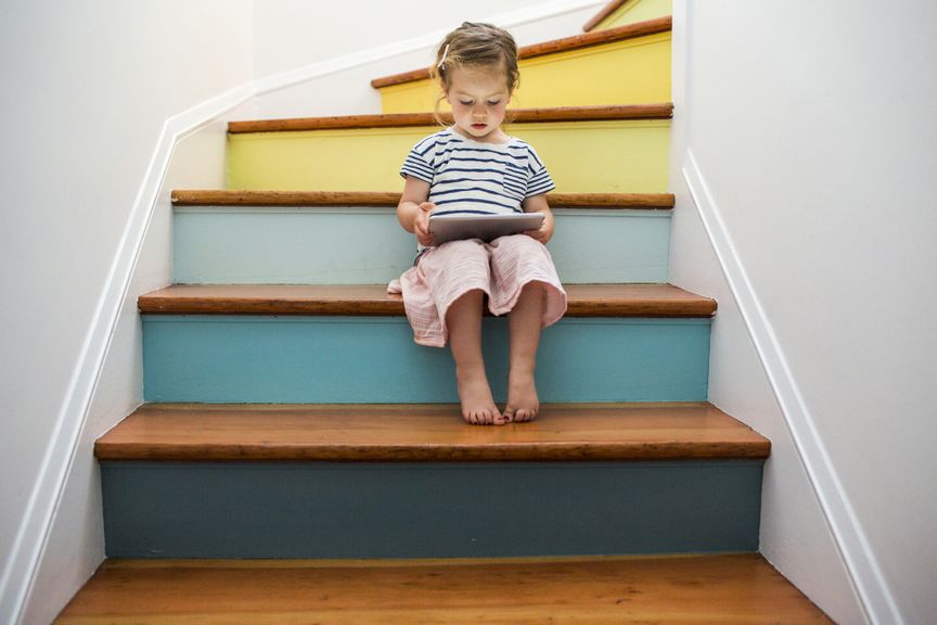 Kind sitzt mit eibem Tablet auf einer bunt gestrichenen Treppe
