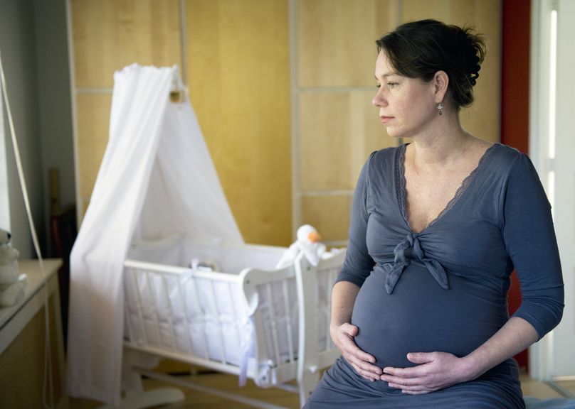 Hochschwangere Frau sitzt nachdenklich vor der Babywiege 