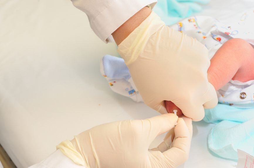 Arzt entnimmt Blut aus der Ferse eines Neugeborenen