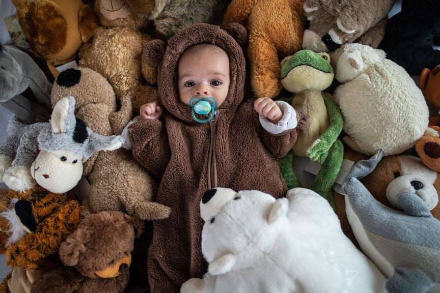 Baby im Bärenkostüm mit vielen Kuscheltieren