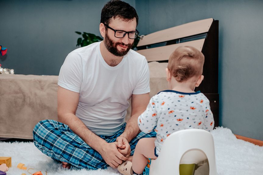 Baby sitzt auf dem Töpfchen und Vater sitzt daneben