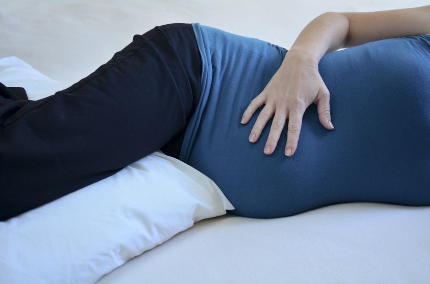 Schwangere liegt auf der Seite mit einem Kissen zwischen den Oberschenkeln,Schwangere liegt seitlich mit Kissen zwischen den Beinen