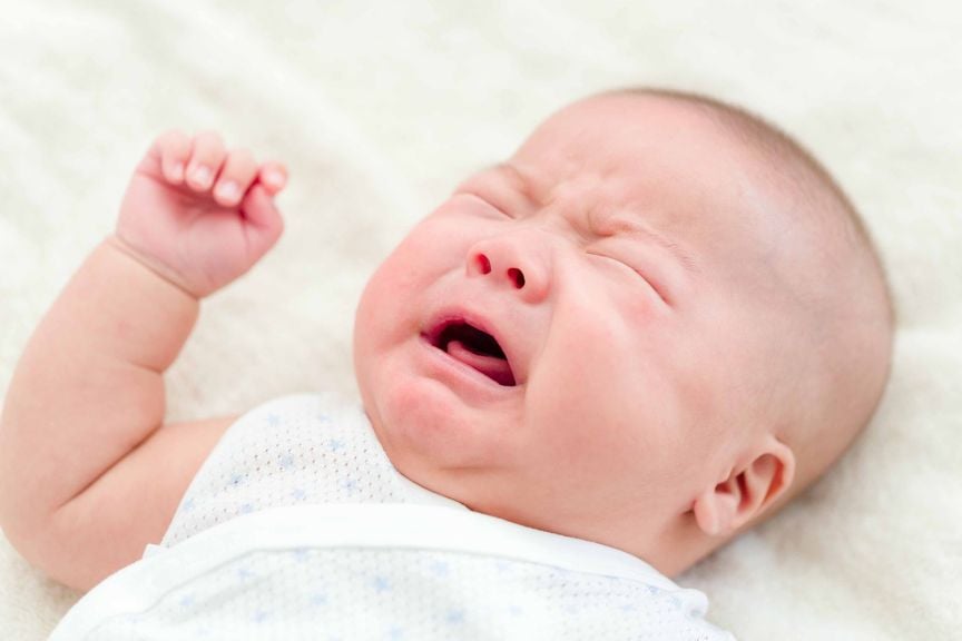 Säugling im Body liegt auf dem Rücken und weint