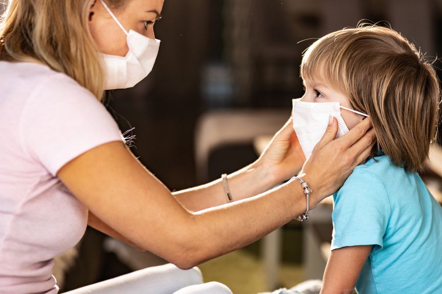Mutter mit Mundschutz legt ihrem Kind die Mund-Nasen-Maske an