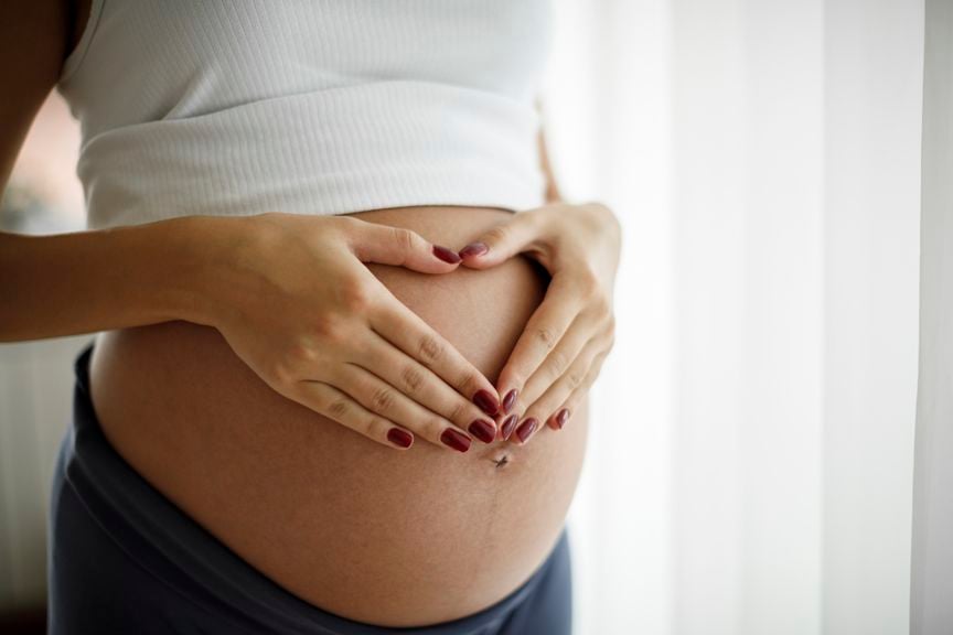 Schwangere legt ihre Hände herzförmig über ihren Babybauch