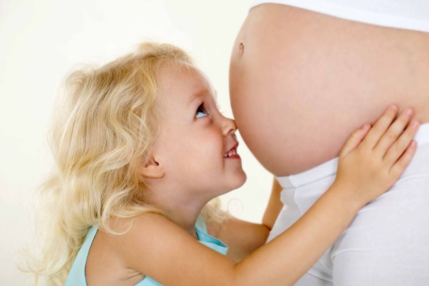 Mädchen stupst mit Nase am Babybauch der Mutter