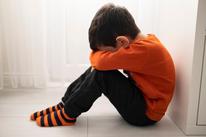 Trauriges Kind sitzt auf dem Fussboden und verbirgt sein Gesicht