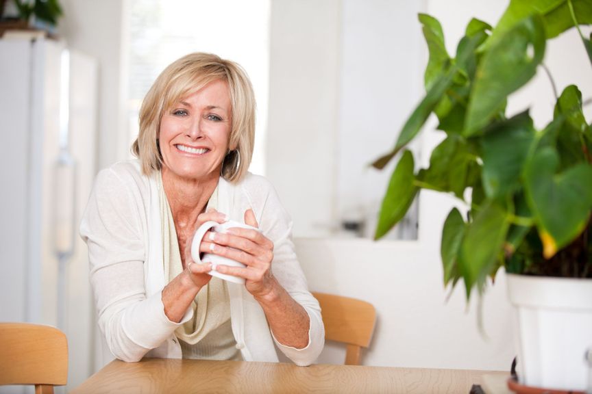 Frau sitzt am Tisch mit einer Tasse in der Hand