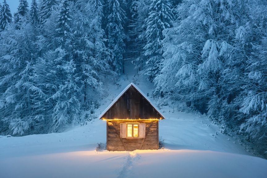 Beleuchtete Holzhütte steht in einer nächtlichen Winterlandschaft