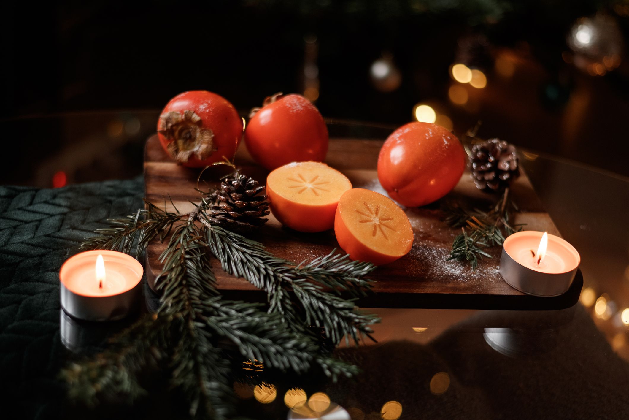 Ganze und aufgeschnittene Kakifrüchte umgeben von Weihnachtsdekoration