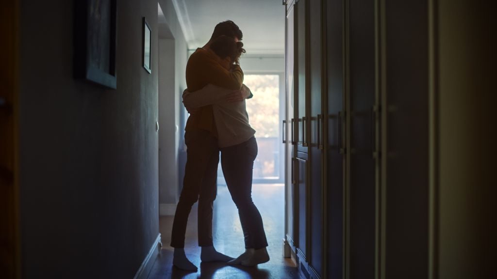 Trauerndes Paar steht in einem dunklen Hausflur und umarmt sich