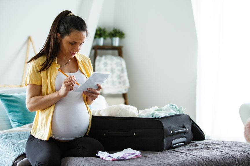 Schwangere packt den Klinikkoffer mit Checkliste in der Hand