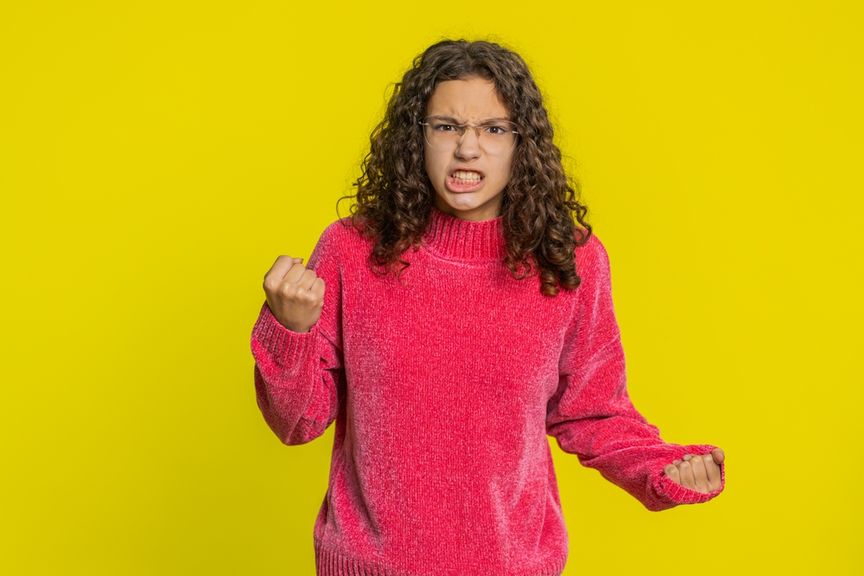 Wütende junge Frau im roten Pullover vor gelbem Hintergrund ballt die Fäuste