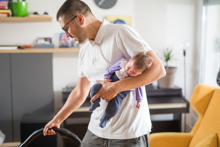 Vater mit Säugling im Arm bei der Hausarbeit
