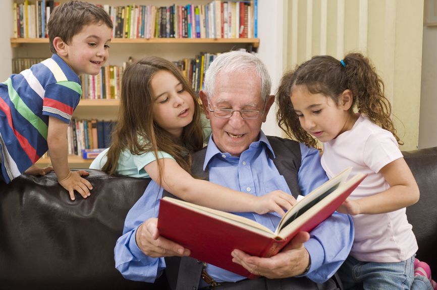 Älterer Mann liest drei Kindern aus einem roten Buch vor
