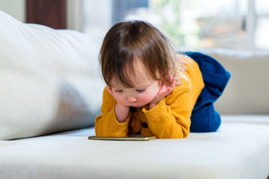 Kind auf dem Sofa schaut auf das Display eines Smartphones