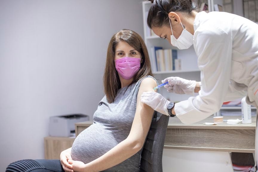 Schwangere Frau mit pinkfarbenem Mundschutz wird gegen Covid-19 geimpft