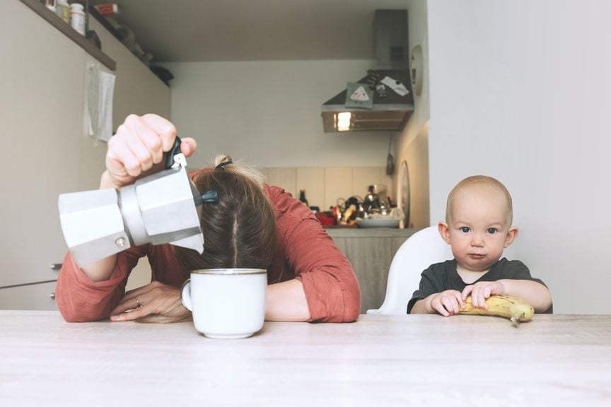 Müde Mutter mit Kaffee und munterem Kind am Tisch