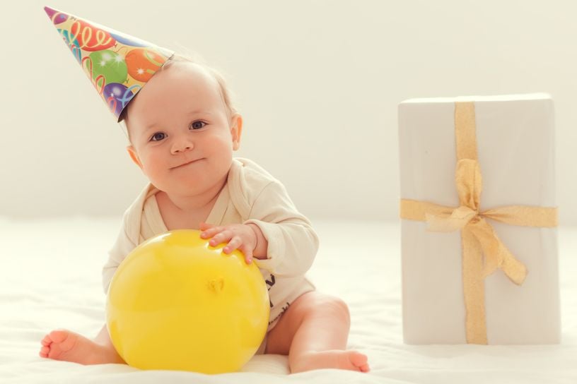 Baby mit Partyhut, Ballon und Geschenk