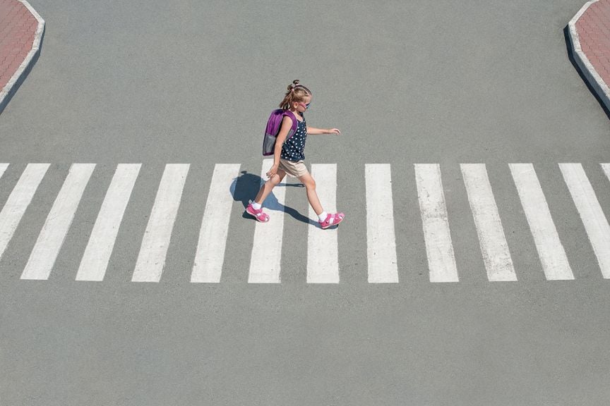 Kind mit Schulrucksack überquert auf dem Zebrastreifen eine Strasse