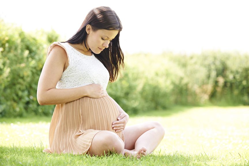 Schwangere sitzt auf einer Wiese mit ihren Händen auf ihrem Bauch