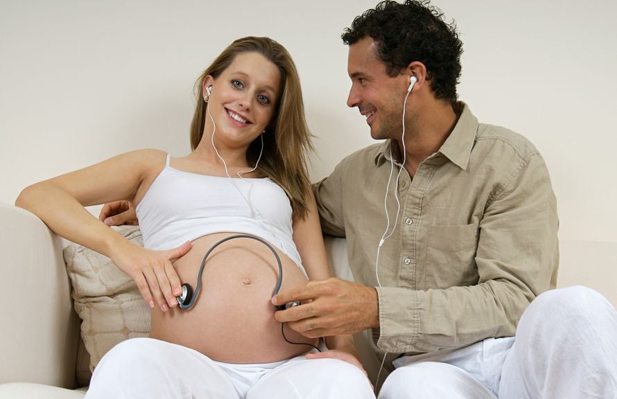 Schwangere mit Partner hält Kopfhörer auf den Babybauch