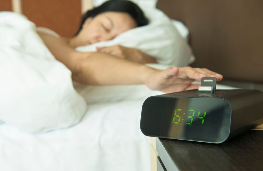 Frau drückt im Halbschlaf die Schlummertaste eines digitalen Weckers