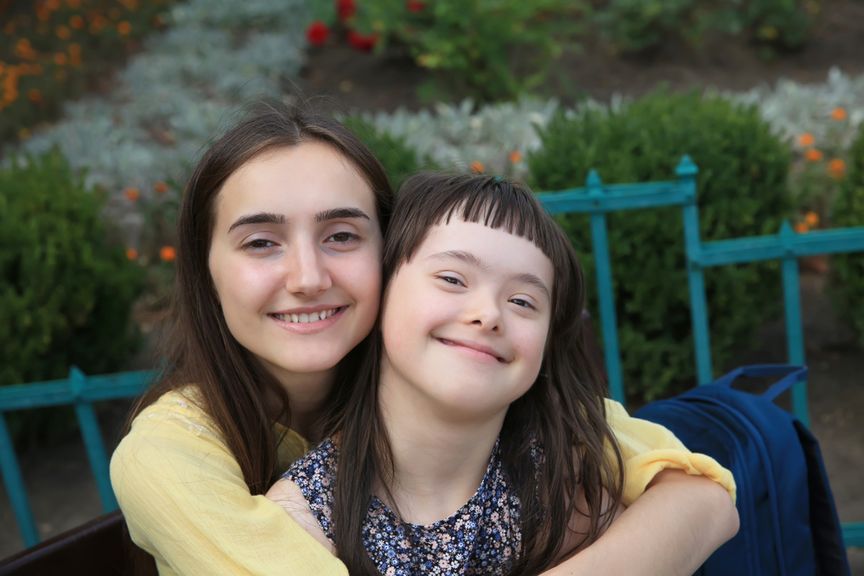 Kind mit Downsyndrom wird von seiner grossen Schwester umarmt