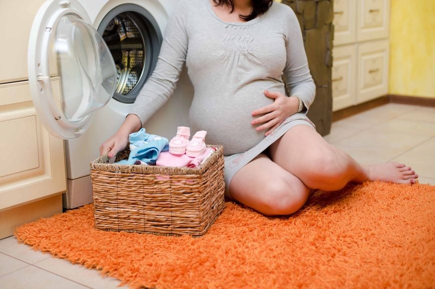 Schwangere sitzt vor der Waschmaschine am Boden