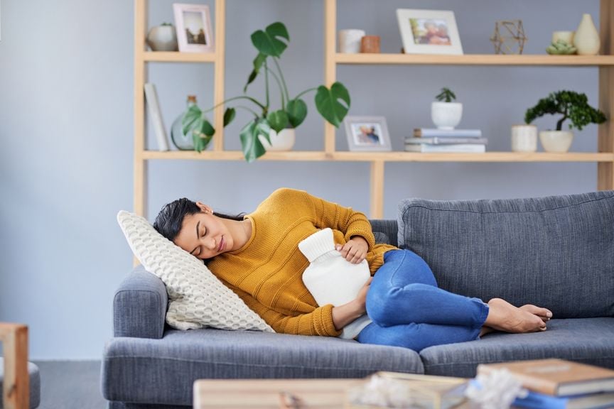 Frau liegt auf dem Sofa mit einer Wärmflasche auf dem Bauch