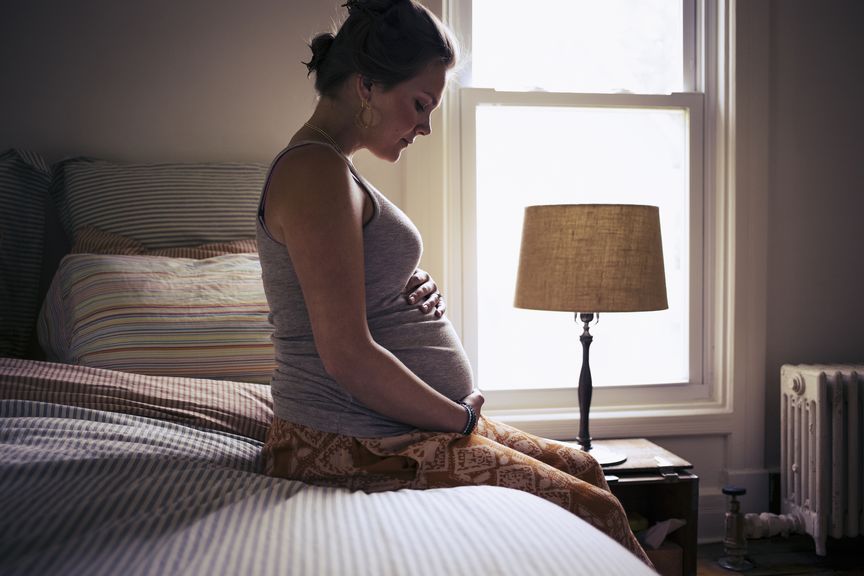 Schwangere sitzt auf dem Bett und hält sich den Bauch