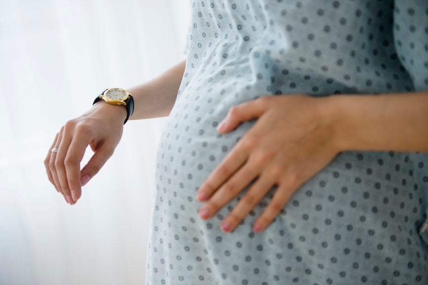 Schwangere zählt auf der Armbanduhr die Minuten zwischen Wehen