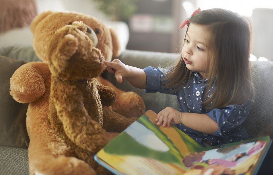 Kind erzählt seinen Teddybären ein Bilderbuch
