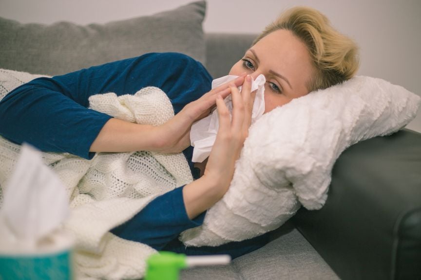 Frau liegt auf dem Sofa und putzt sich die Nase