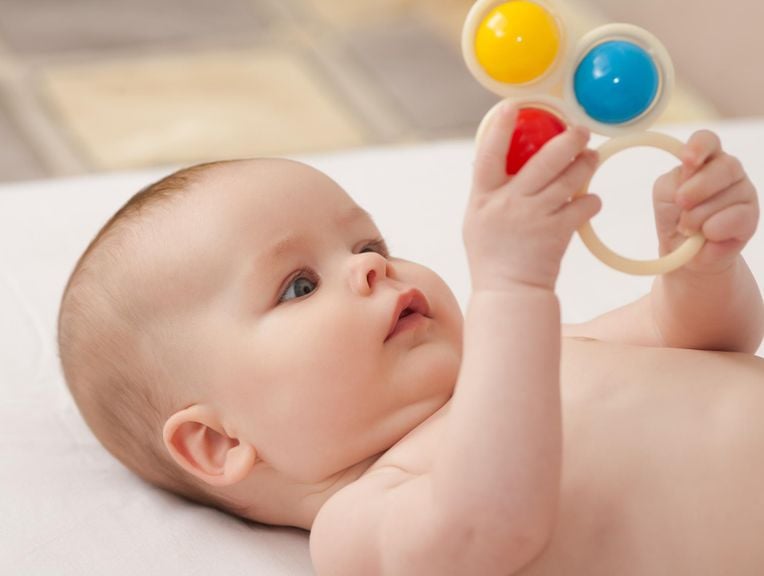 nacktes Baby liegt auf dem Rücken und spielt mit einem Kugelring