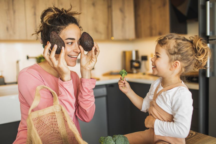 Mutter und Kind nach dem Einkaufen in der Küche mit Avocados und Broccoli