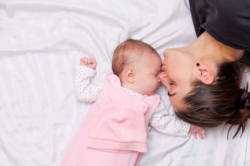 Mutter und Baby im Elternbett, Mutter küsst Baby auf die Stirn