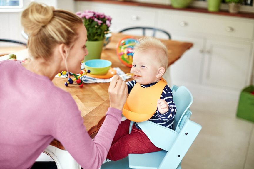 Mutter füttert Baby mit Brei am Esstisch