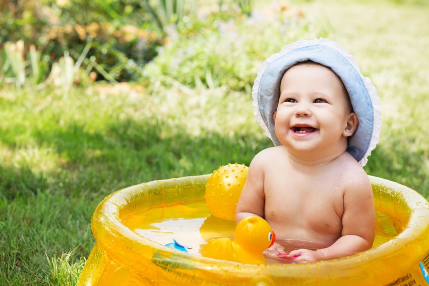 Baby mit Sonnenhut im aufblasbaren Planschbecken mit Spielsachen