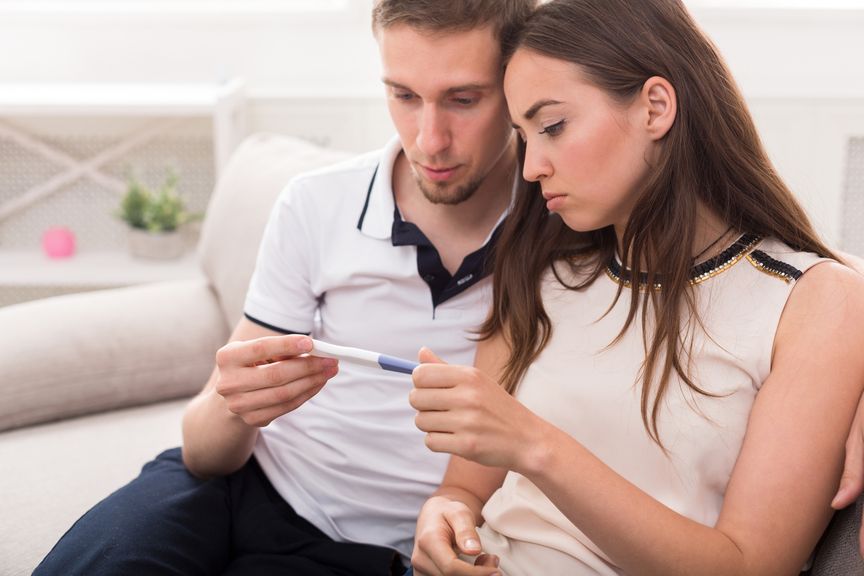 Paar hält Schwangerschaftstest in den Händen, enttäuscht, abwartend