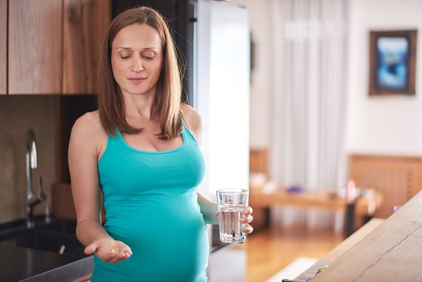 Schwangere mit Wasserglas und Vitaminkapseln in der Hand 