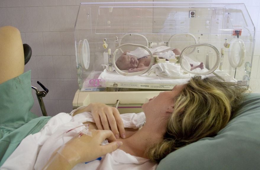 Mutter liegt neben dem Inkubator mit ihrem Kind