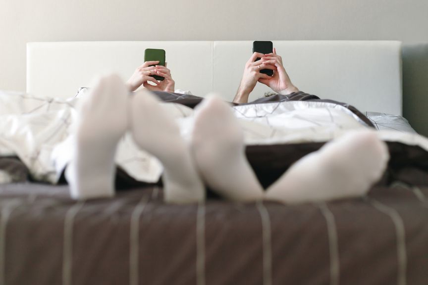 Frau und Mann liegen auf dem Rücken im Bett, beide mit einem Smartphone in den Händen