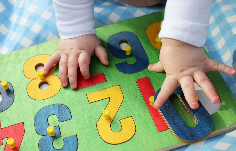 Babyhände auf einer bunten Holzplatte mit Zahlen