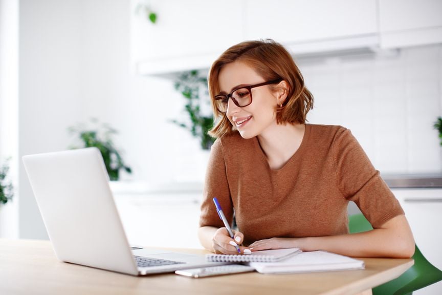 Frau sitzt am Laptop und macht sich Notizen