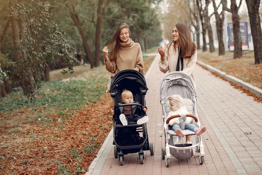 Zwei Frauen mit ihren Babys im Buggy spazieren im Park und reden miteinander